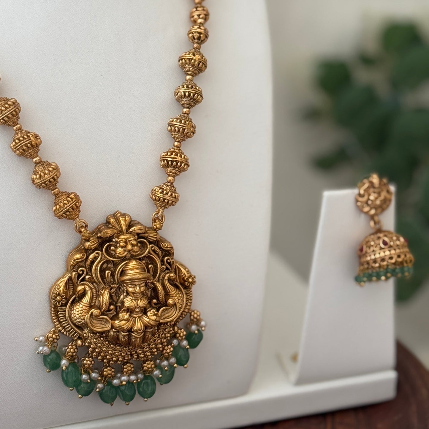 Gold necklace with green beads and a white background