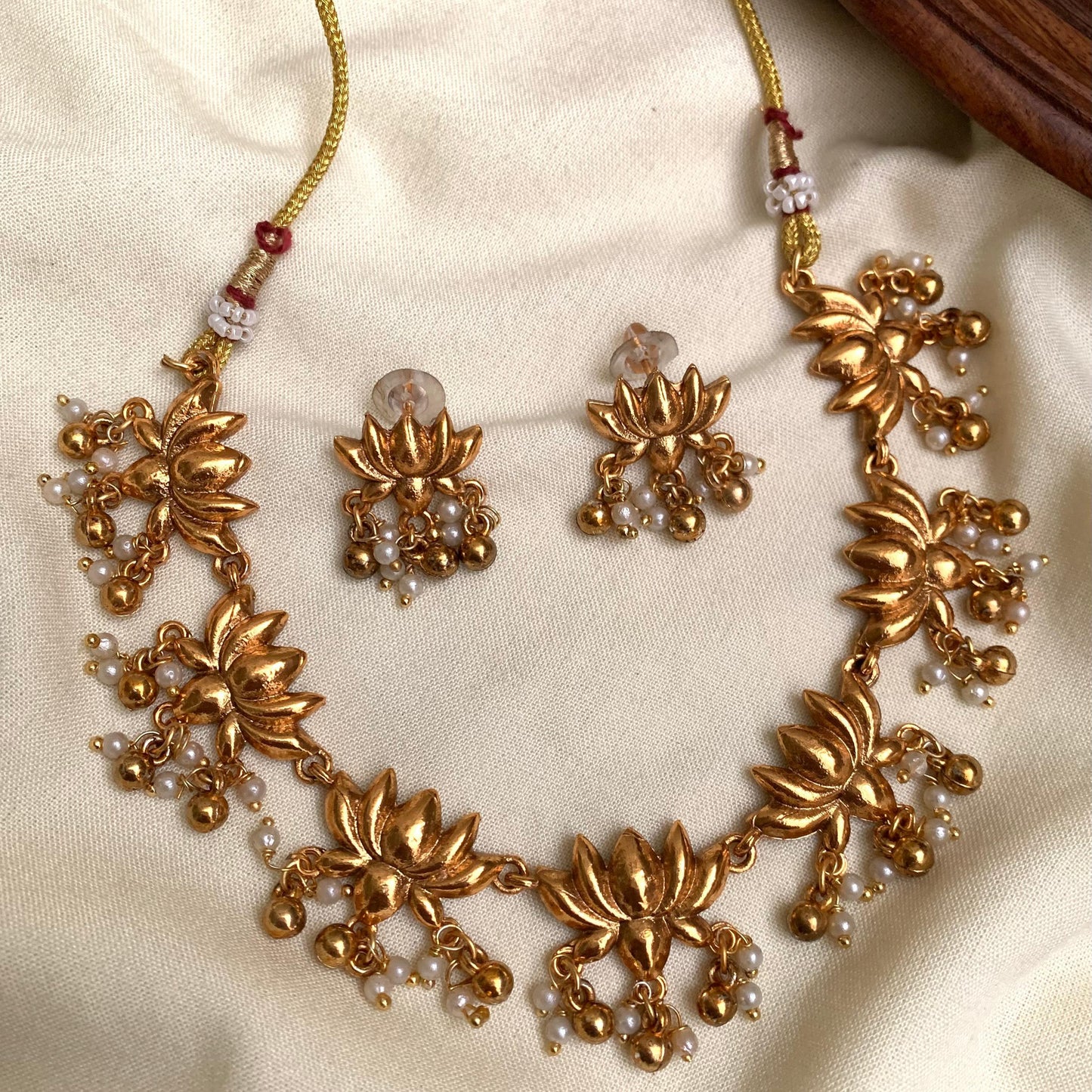 Gold necklace and earrings set on a beige fabric background