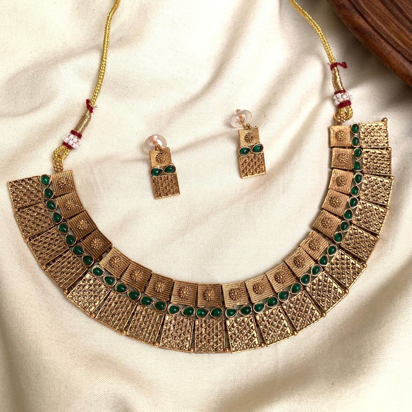 Gold necklace with green gemstones on a beige fabric background