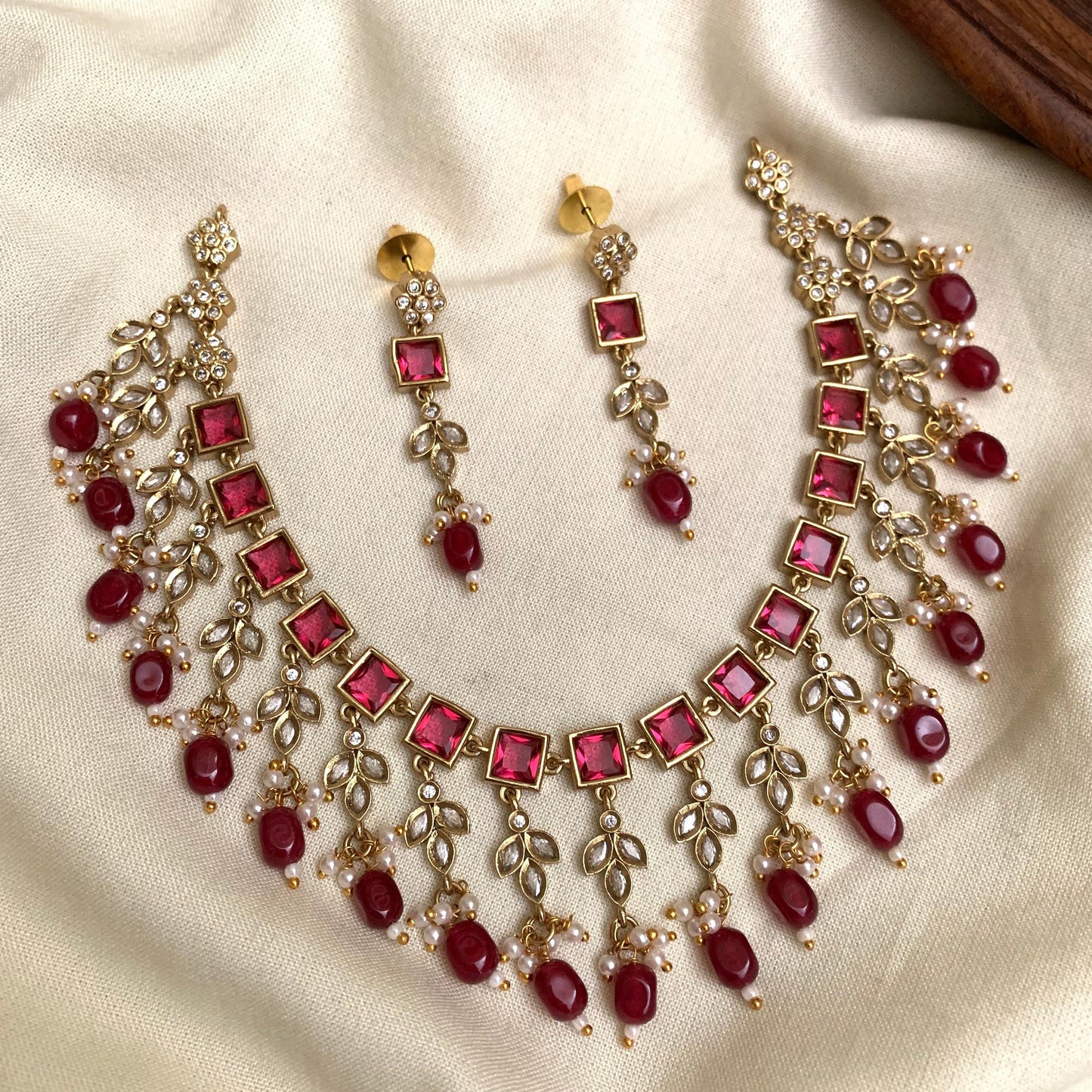 Necklace and earrings set with red gemstones on a beige fabric background