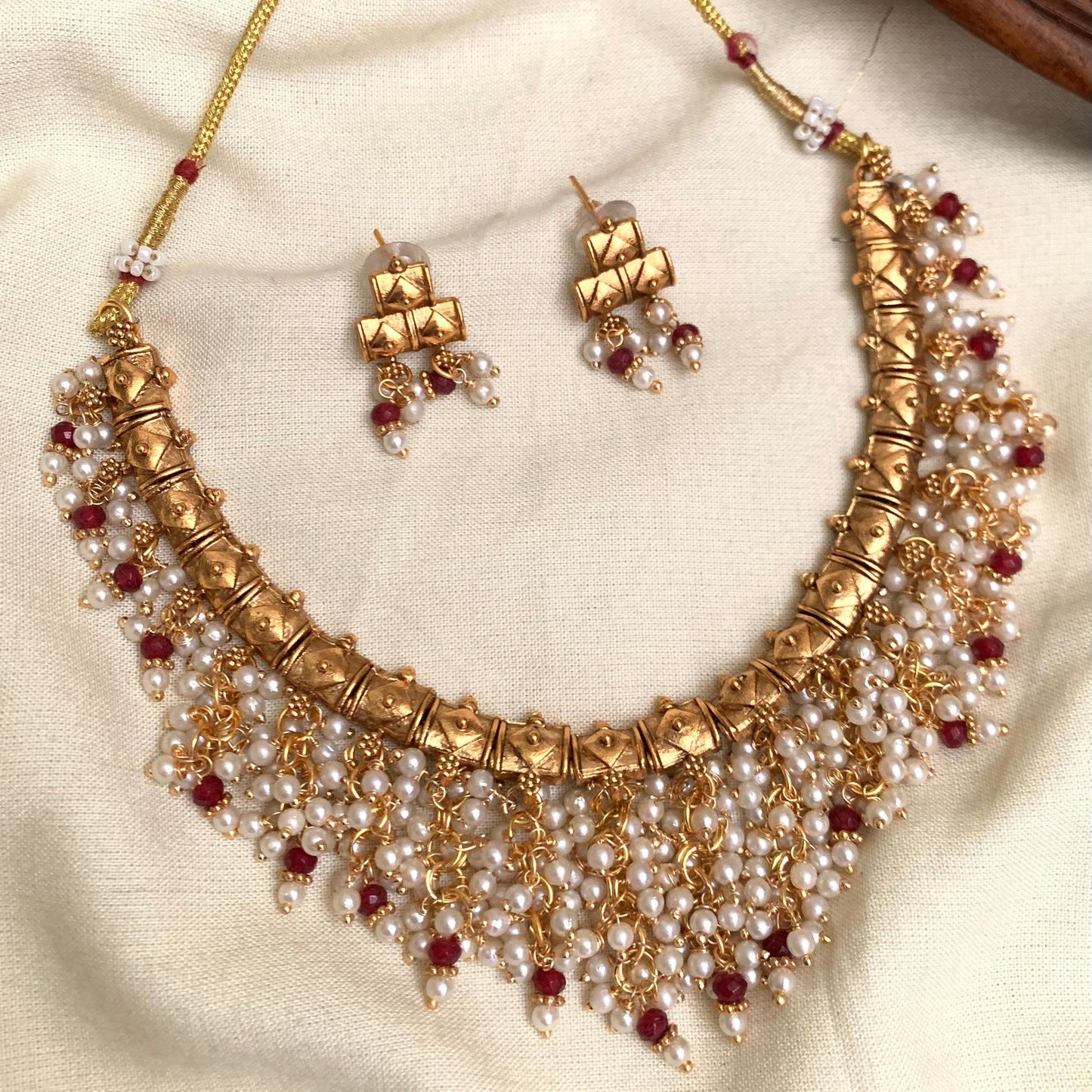 Gold necklace with pearls and red stones on a beige fabric background