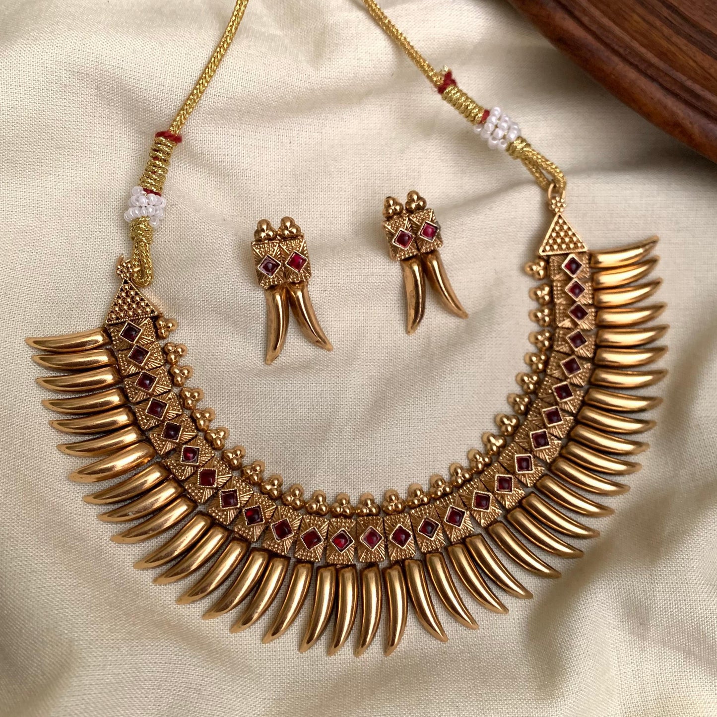Gold necklace and earrings set on a beige fabric background
