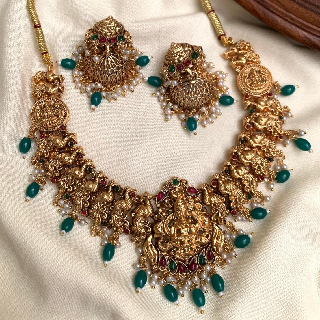 Ornate gold necklace with green and red stones on a white fabric background