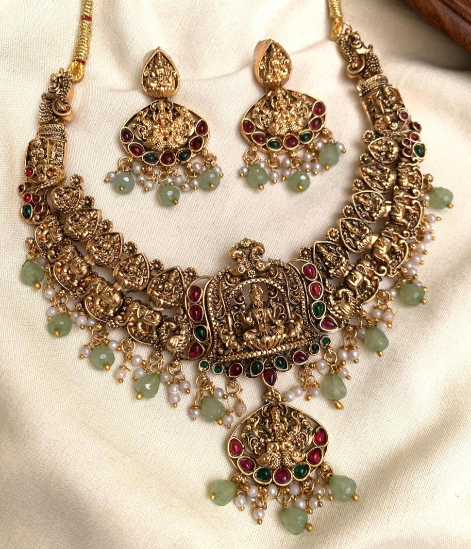Ornate gold necklace with green and red stones on a white fabric background