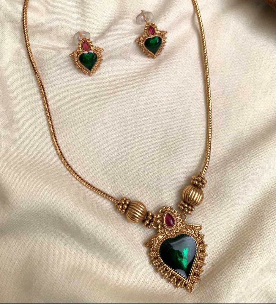 Gold necklace with green gemstones on a beige fabric background