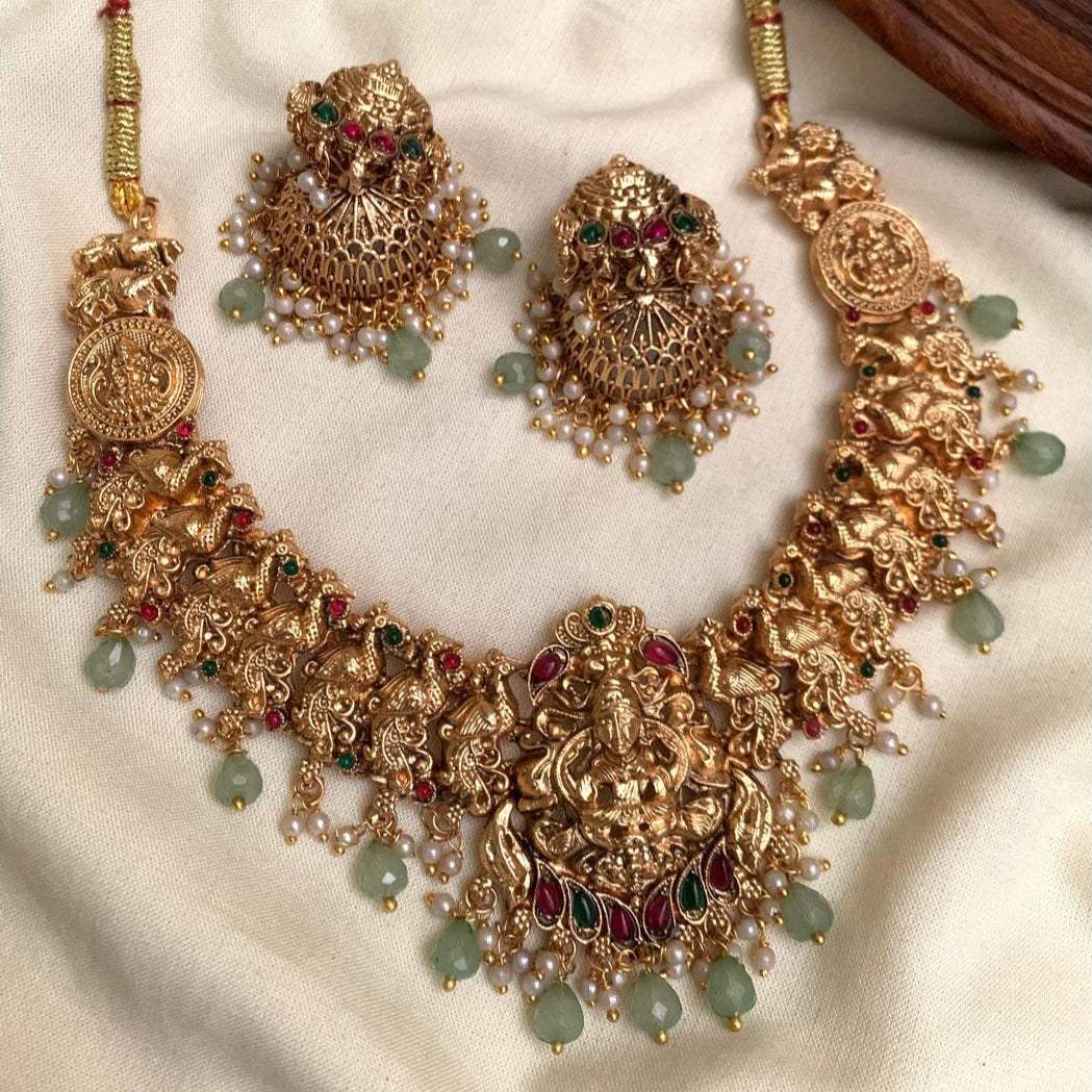 Ornate gold necklace with green beads and red stones on a white fabric background