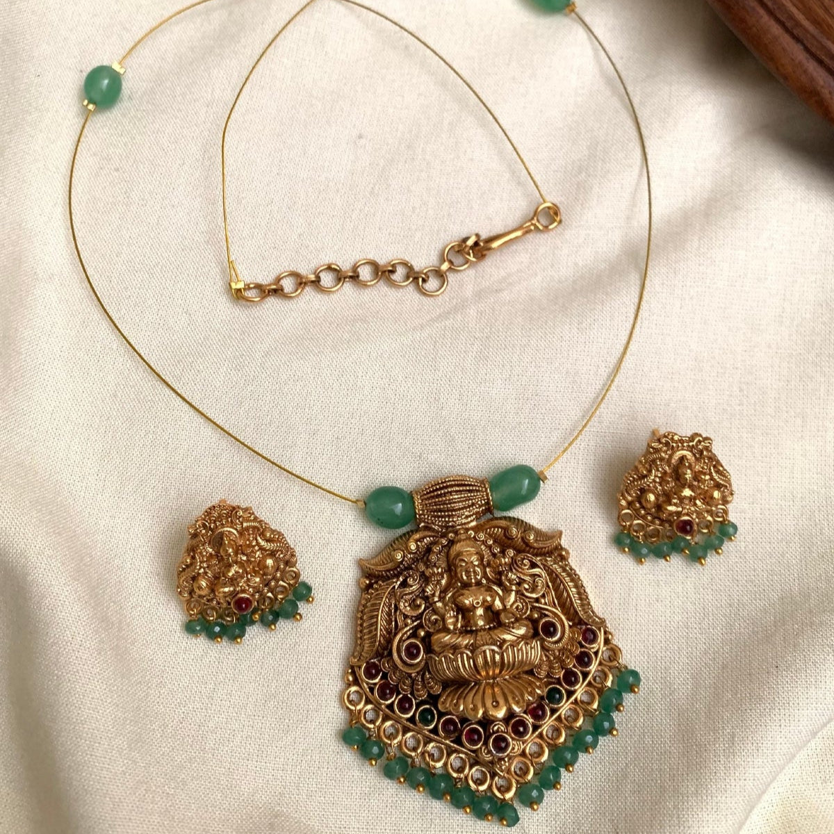 Gold necklace with red beads and matching earrings on a white fabric background