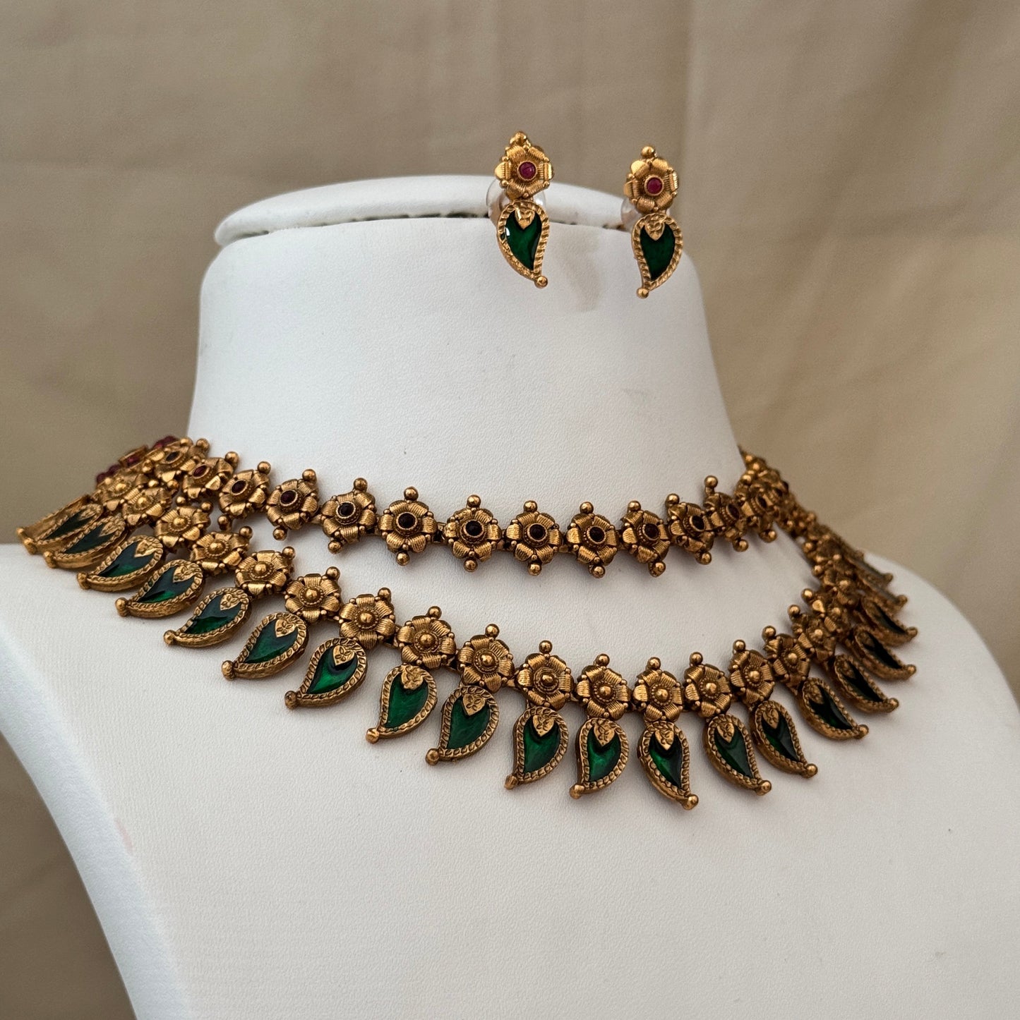 Gold necklace with green stones and matching earrings on a mannequin bust.
