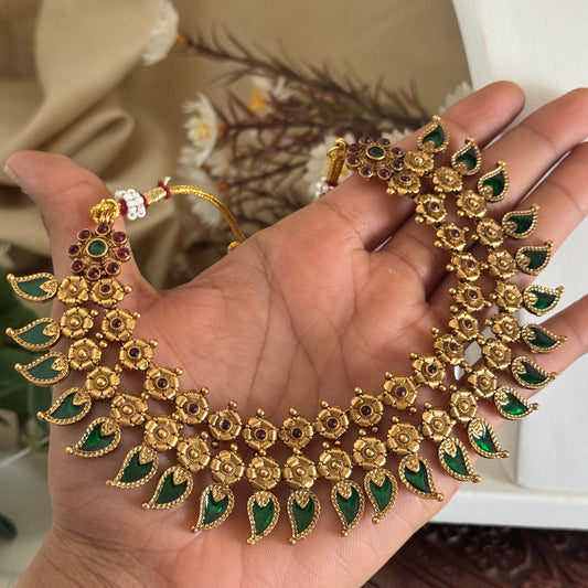 Gold and green floral necklace held in a hand with a blurred background