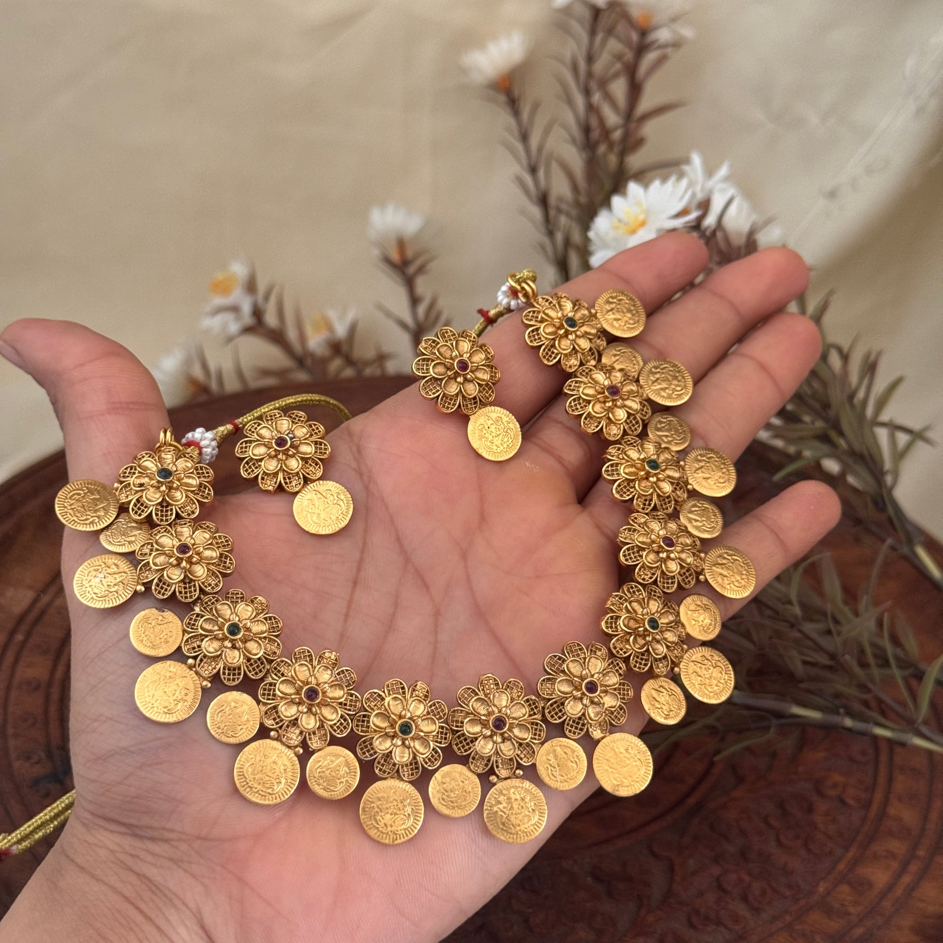Gold necklace held in a hand with a neutral background