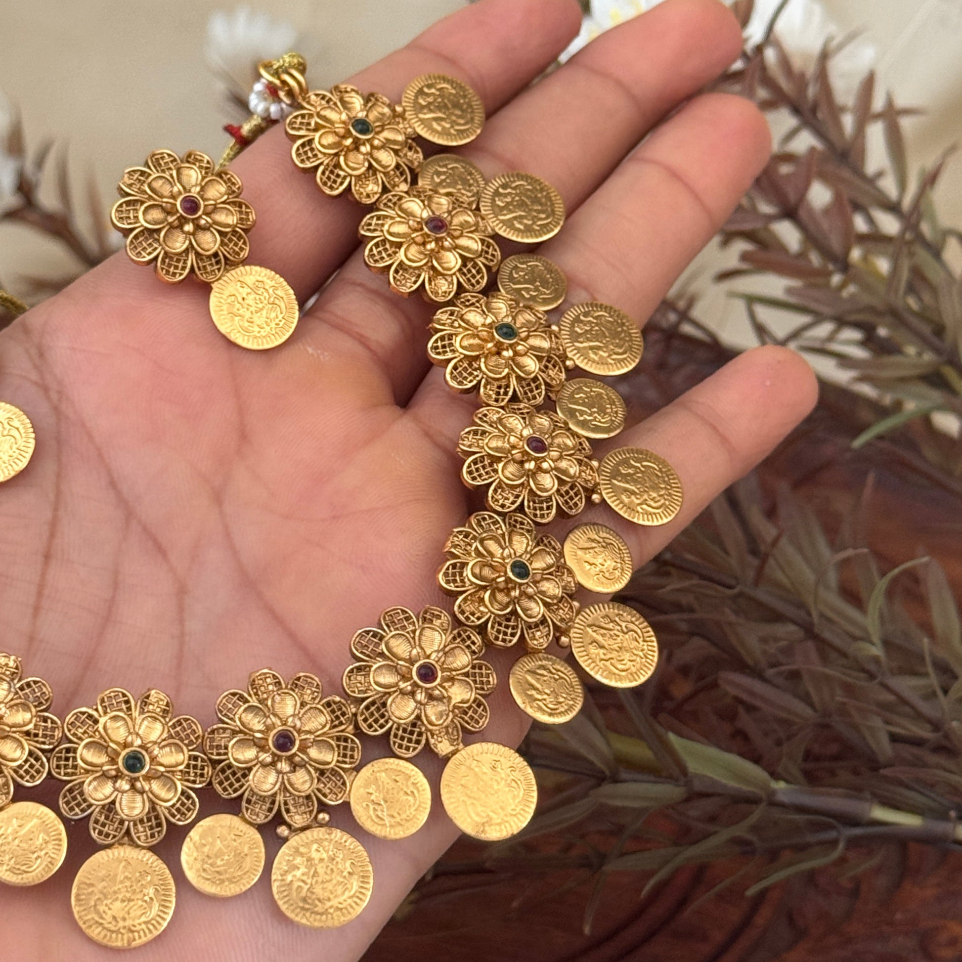 Gold bracelet with floral designs held in a hand against a neutral background