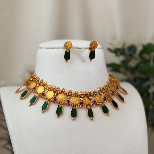 Gold necklace with green and red accents on a white mannequin bust.