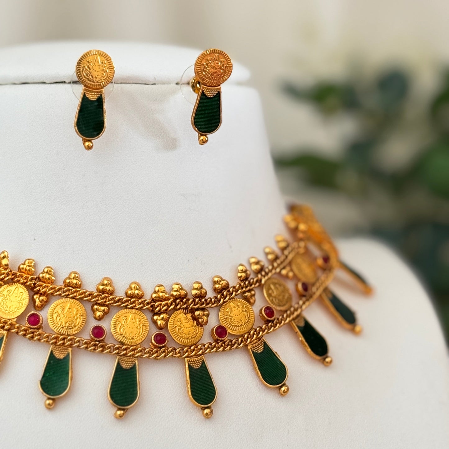 Gold necklace with green and red accents on a mannequin bust.