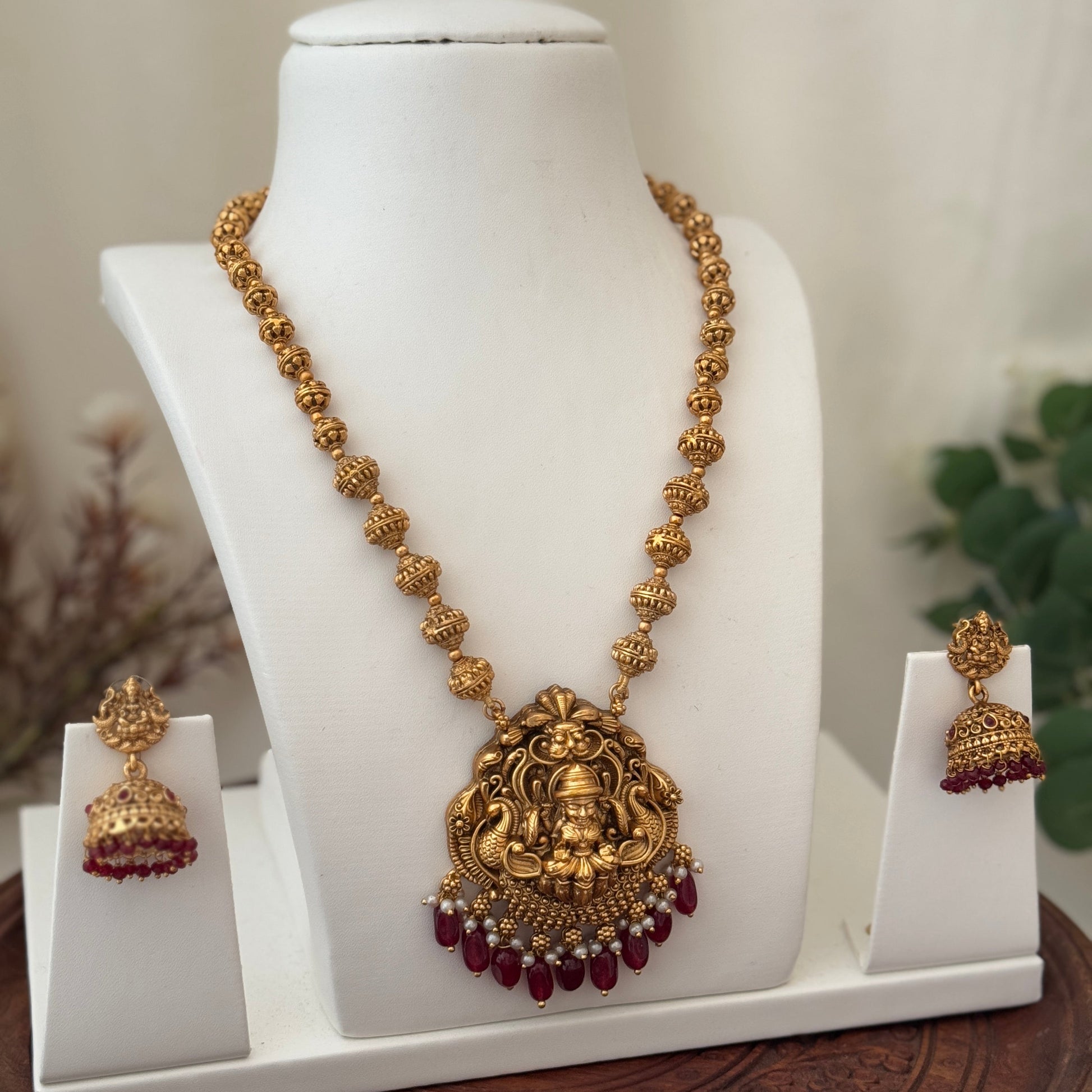 Gold necklace with a large pendant and matching earrings on a white mannequin bust.