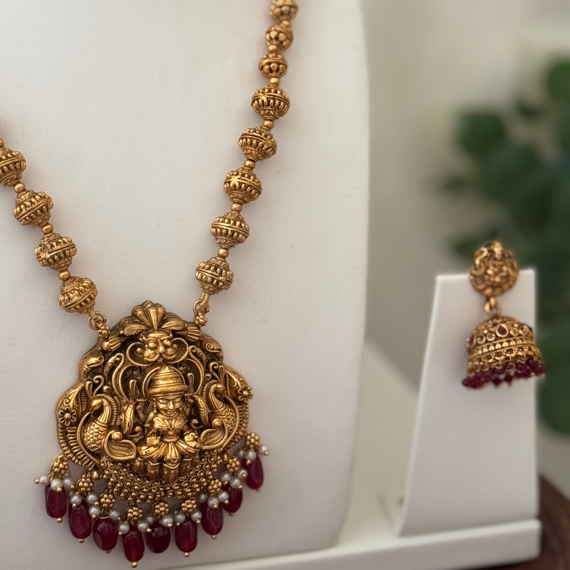 Gold necklace with red beads on a white stand