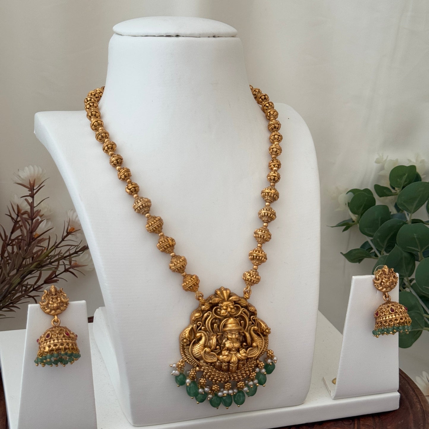 Gold necklace with green stones and matching earrings on a white stand.