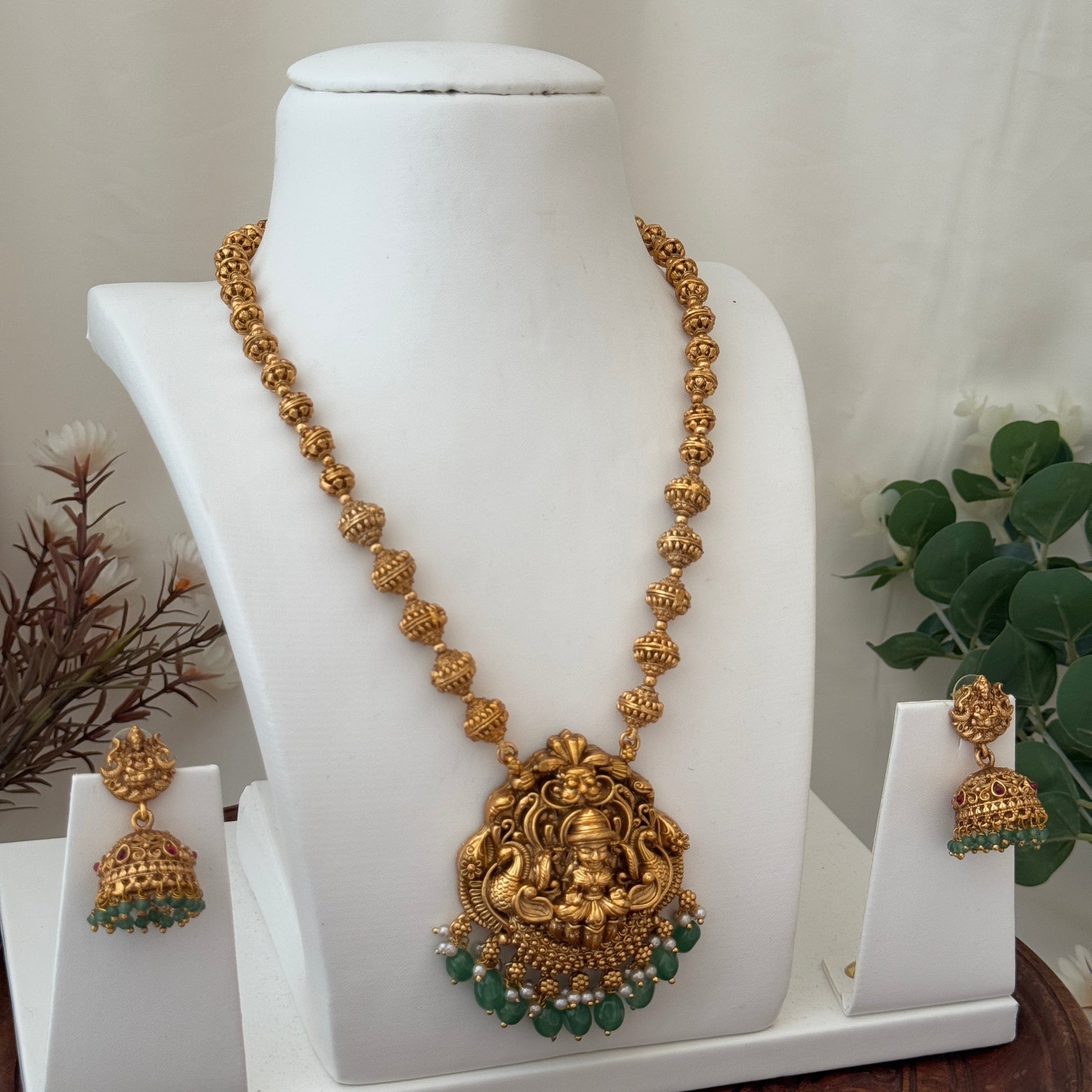 Gold necklace with green stones and matching earrings on a white stand.