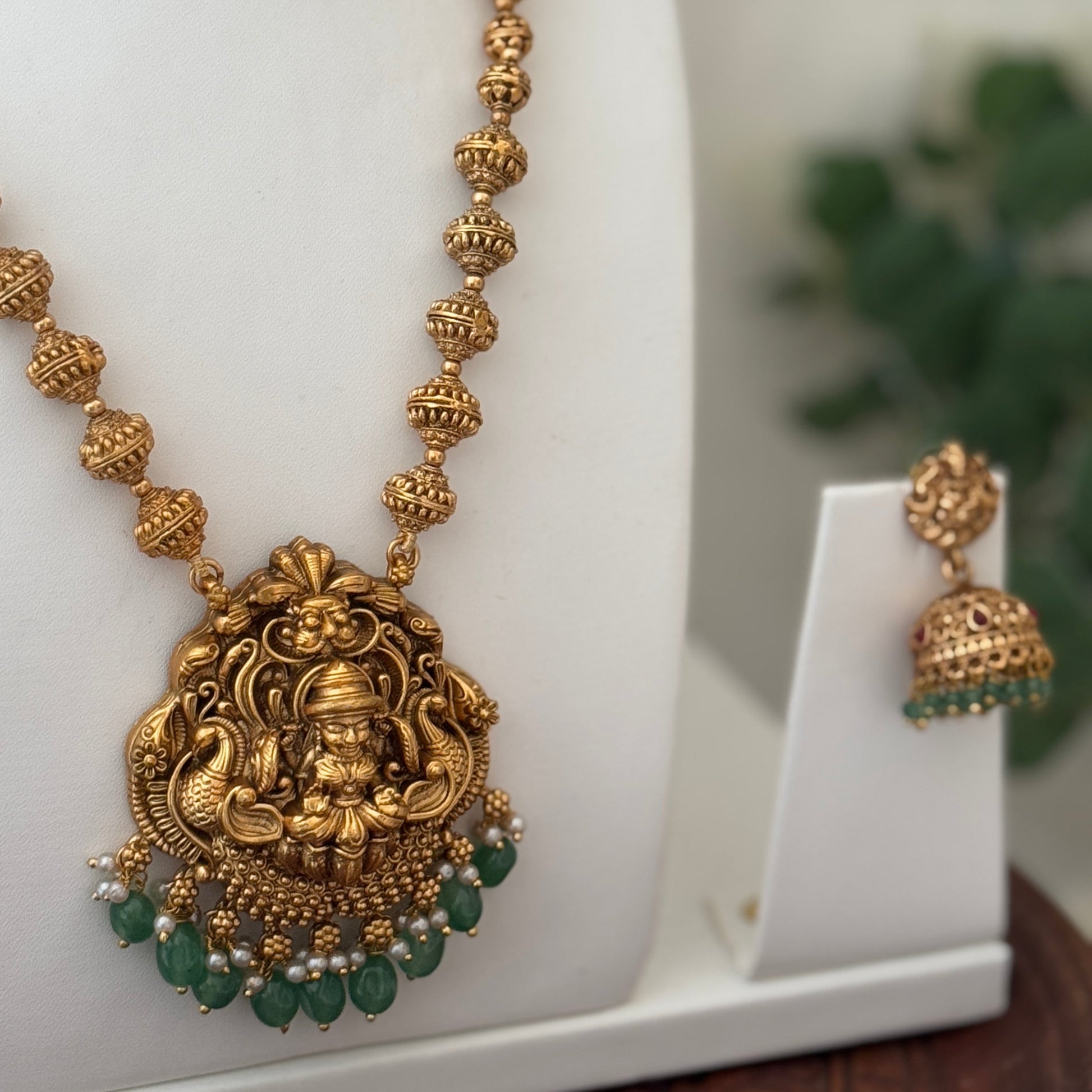 Gold necklace with green beads and a white background