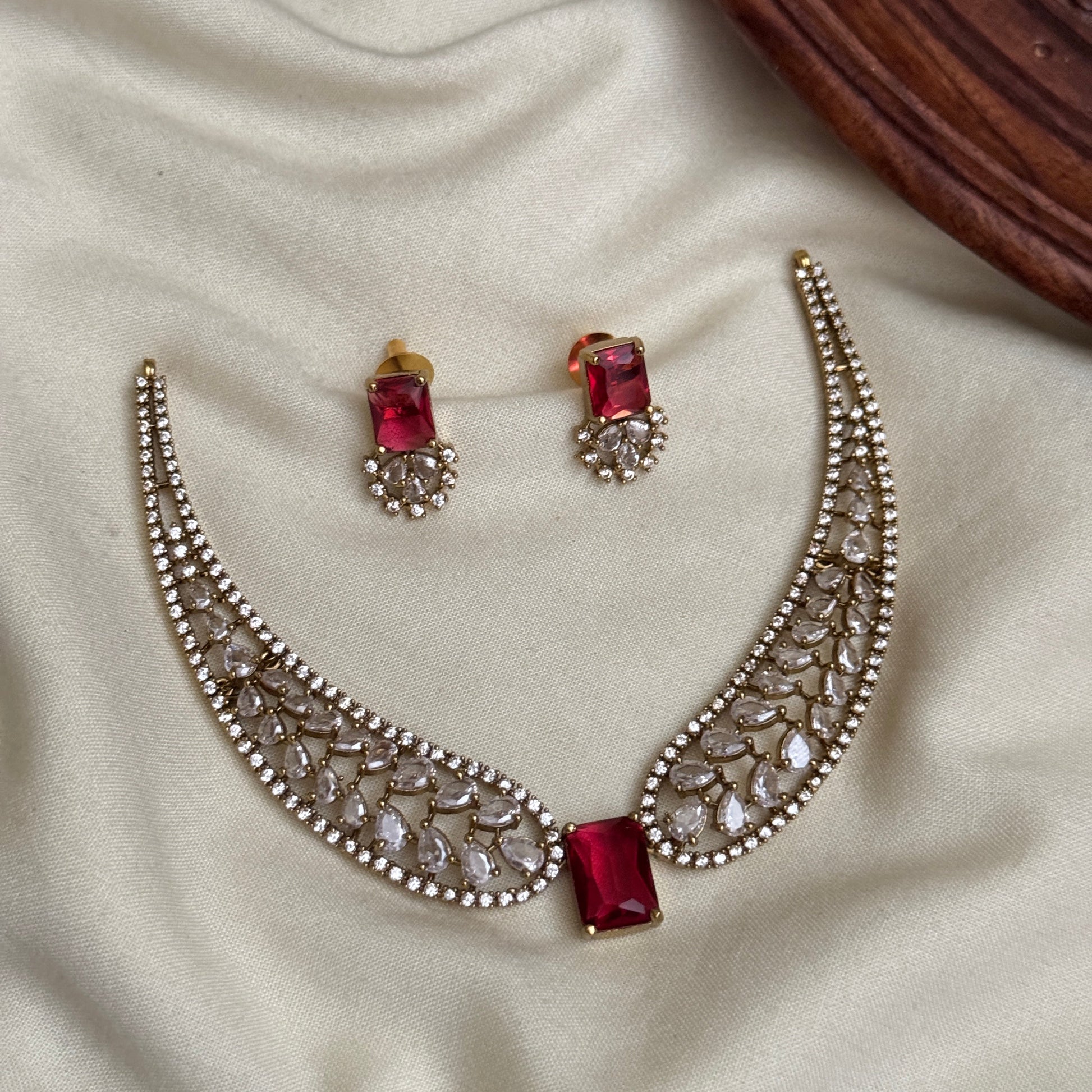Jewelry set with crescent moon design and red gemstones on a beige fabric background