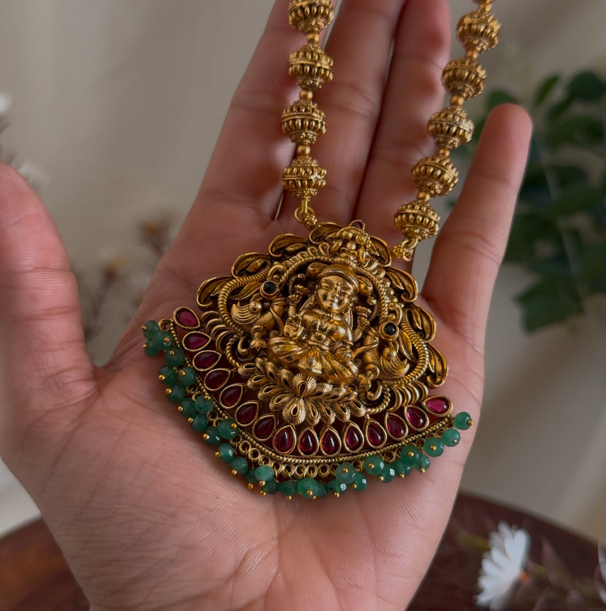 Gold necklace with intricate design held in a hand against a blurred background