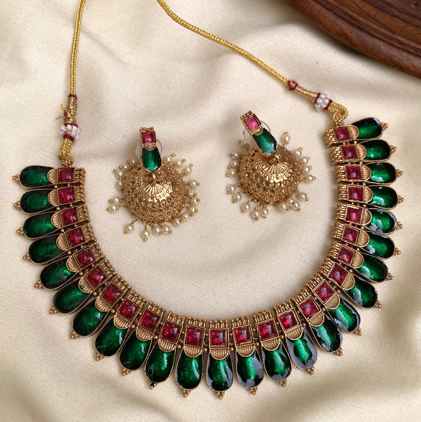 Ornate necklace with green and red stones on a beige fabric background