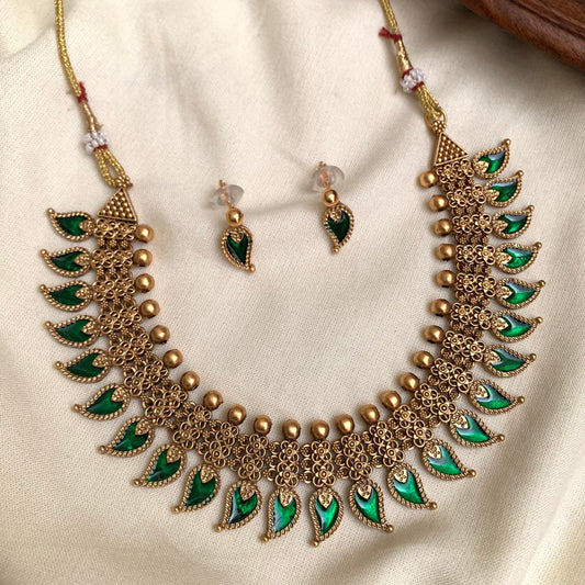 Ornate gold and green necklace with matching earrings on a beige fabric background