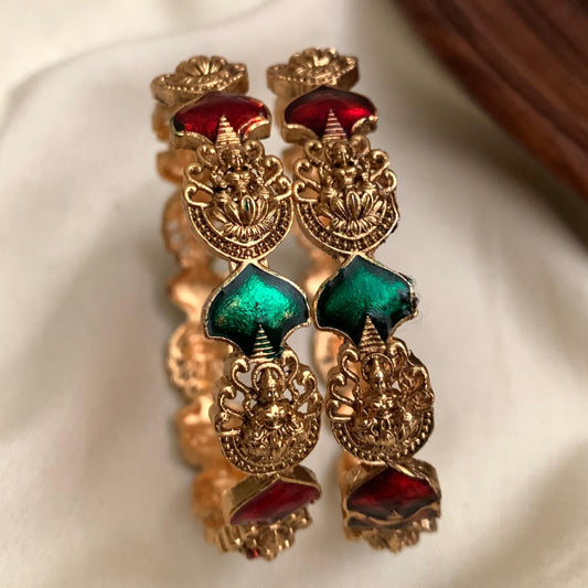 Ornate gold earrings with red and green stones on a beige fabric background