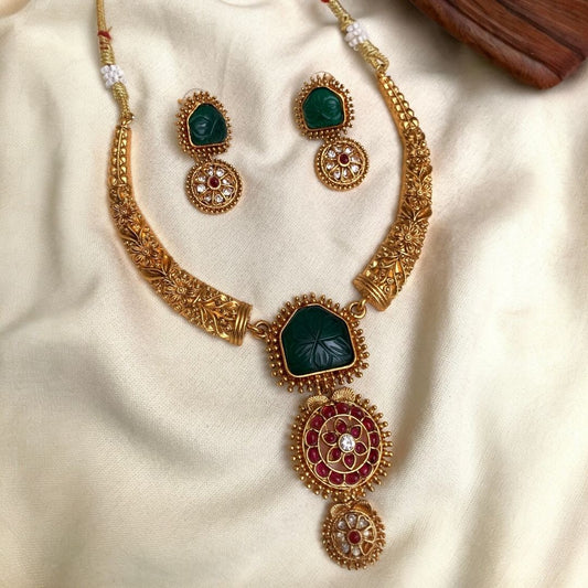 Gold necklace with green and red stones on a beige fabric background