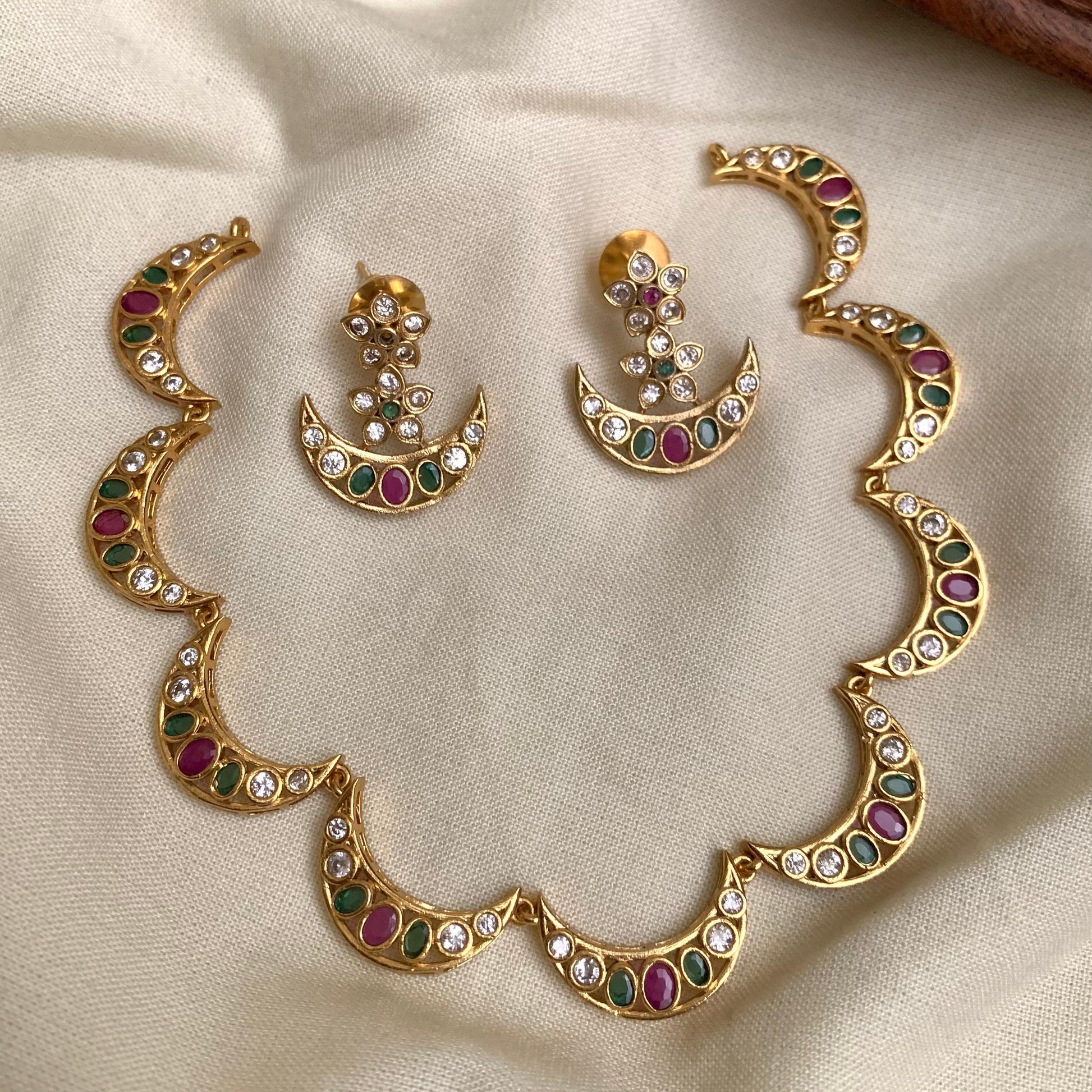 Gold necklace and earrings set with gemstones on a beige fabric background