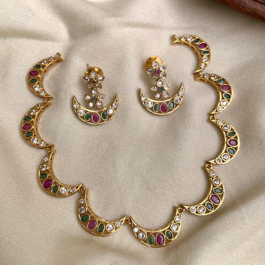 Gold necklace and earrings set with gemstones on a beige fabric background