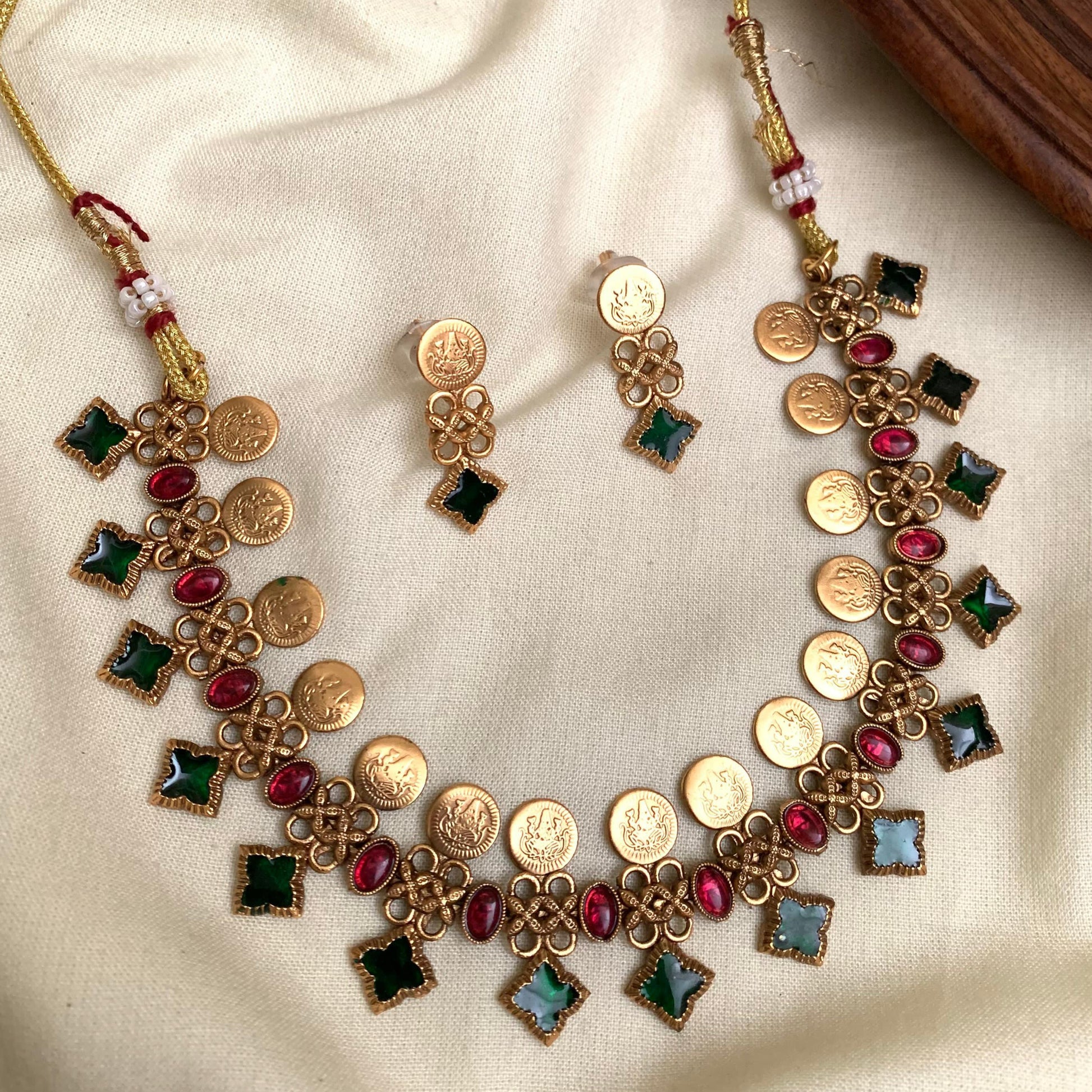 Gold necklace and earrings with colorful stones on a beige fabric background
