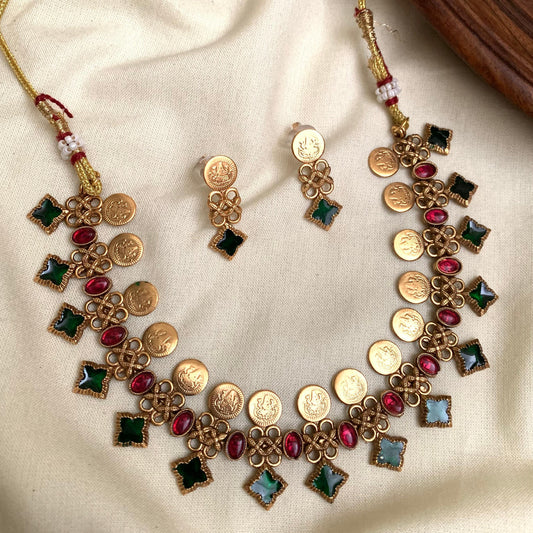 Gold necklace and earrings with colorful stones on a beige fabric background