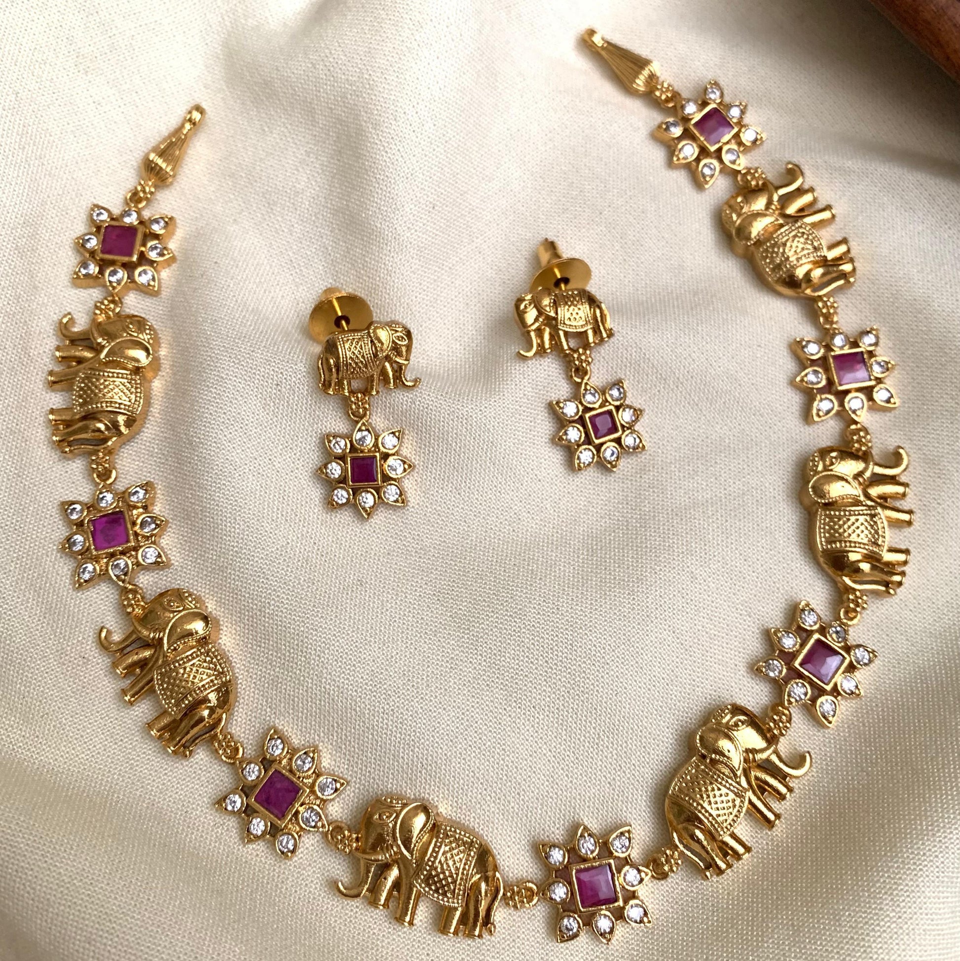 Gold elephant-themed necklace and earrings on a beige fabric background