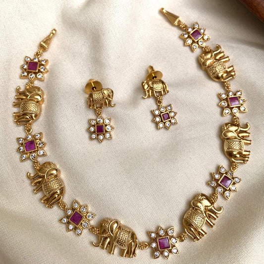 Gold elephant-themed necklace and earrings on a beige fabric background
