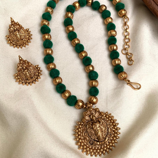 Green beaded necklace with gold accents and intricate pendant on a white fabric background