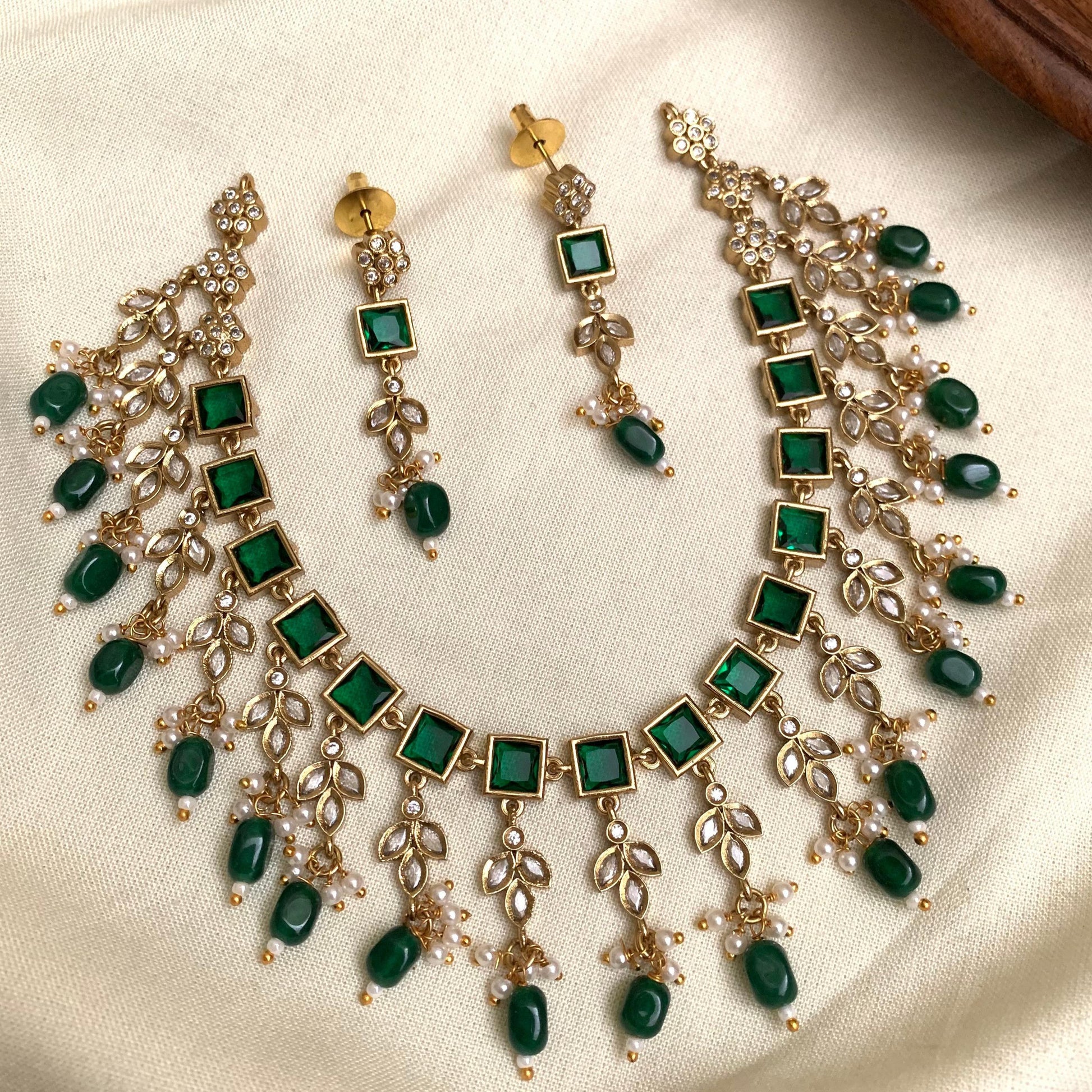 Jewelry set with necklace and earrings featuring green gemstones on a beige fabric background