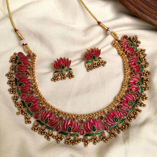 Ornate necklace and earrings set with pink and green details on a beige fabric background