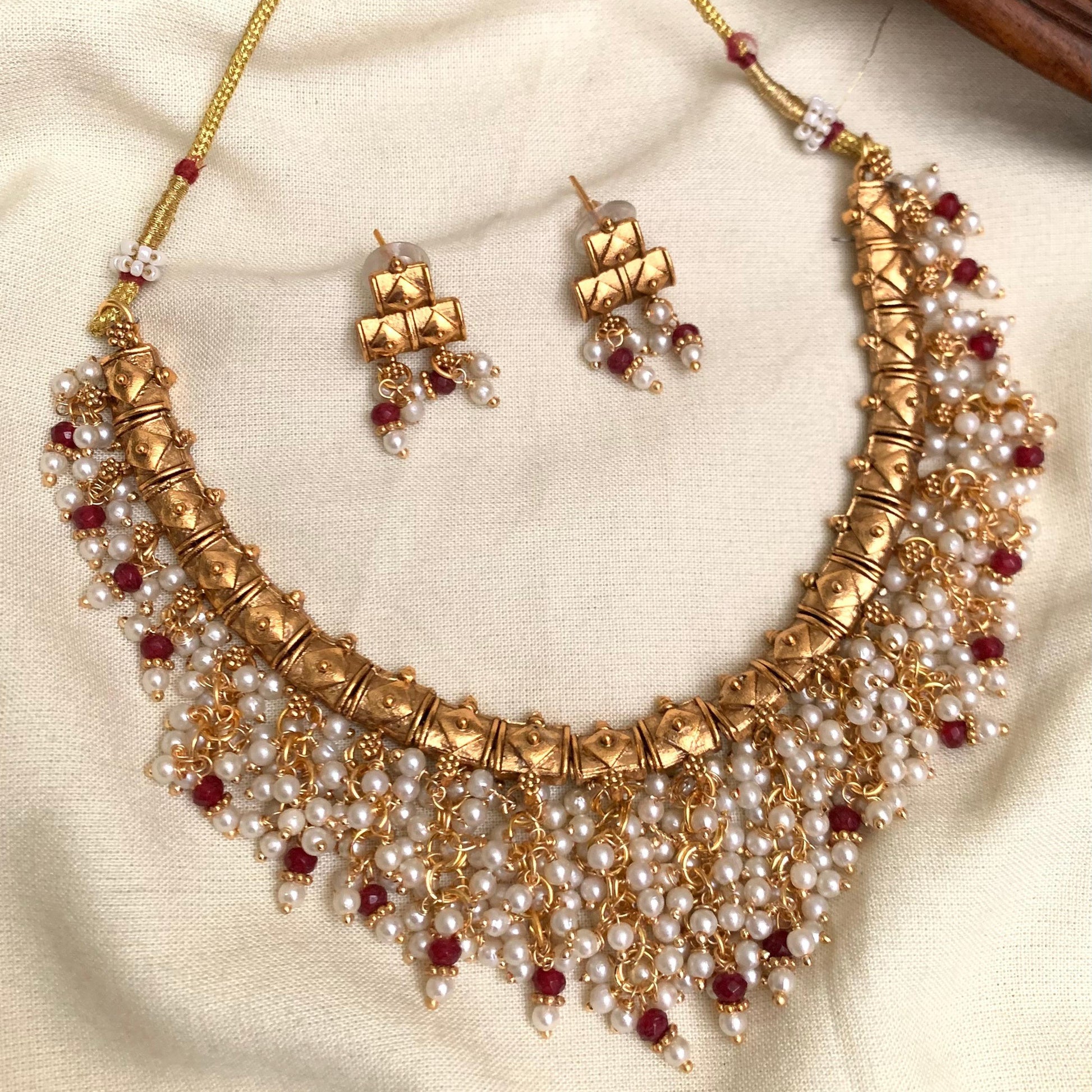 Gold necklace with pearls and red stones on a beige fabric background
