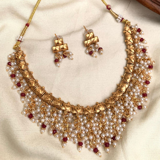 Gold necklace with pearls and red stones on a beige fabric background