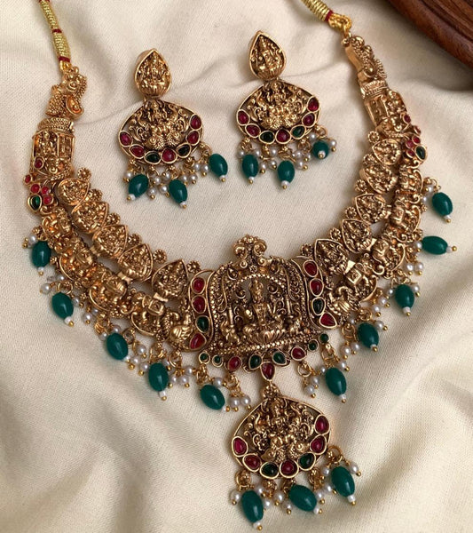 Ornate gold necklace with red and green gemstones on a white fabric background