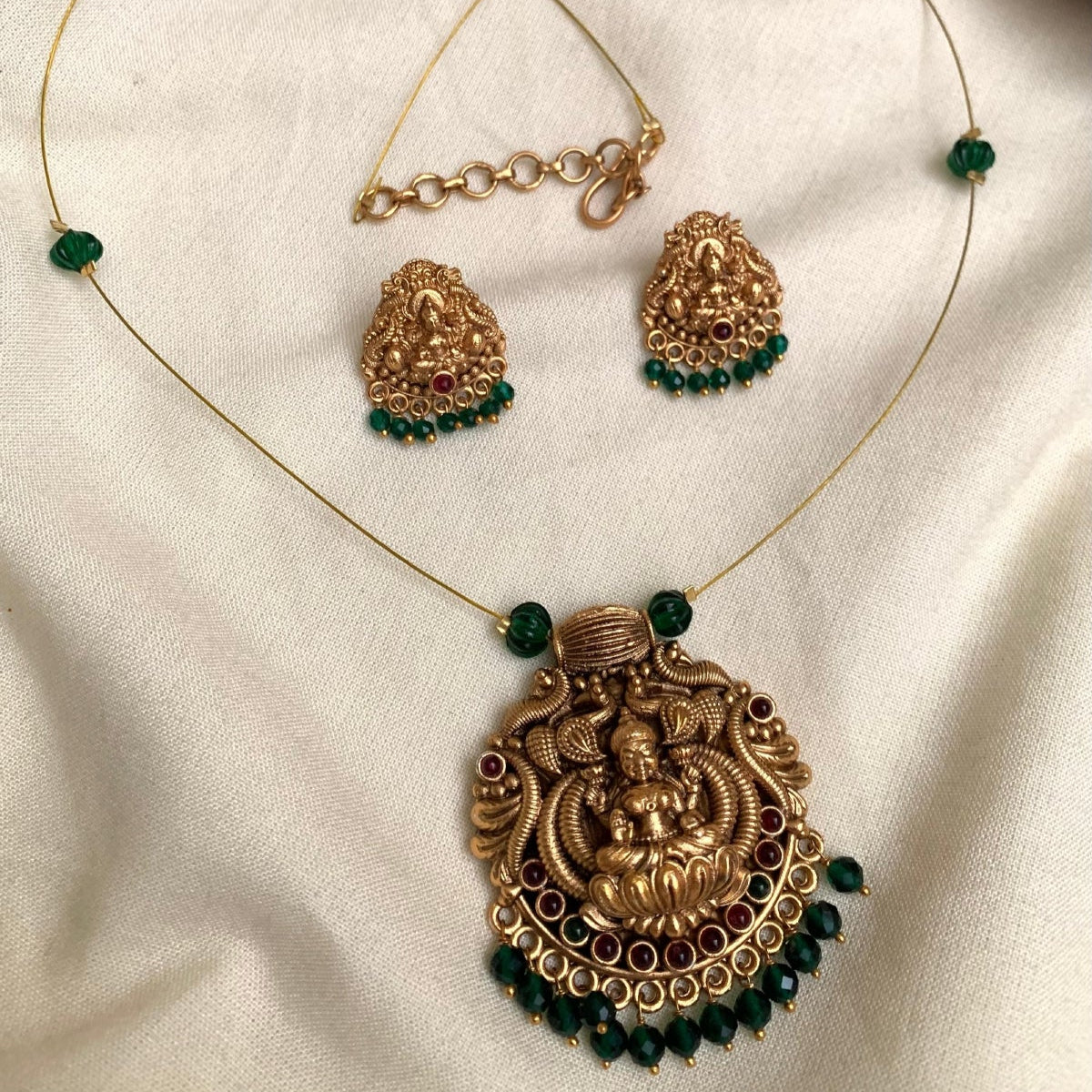 Gold necklace with green beads on a white fabric background