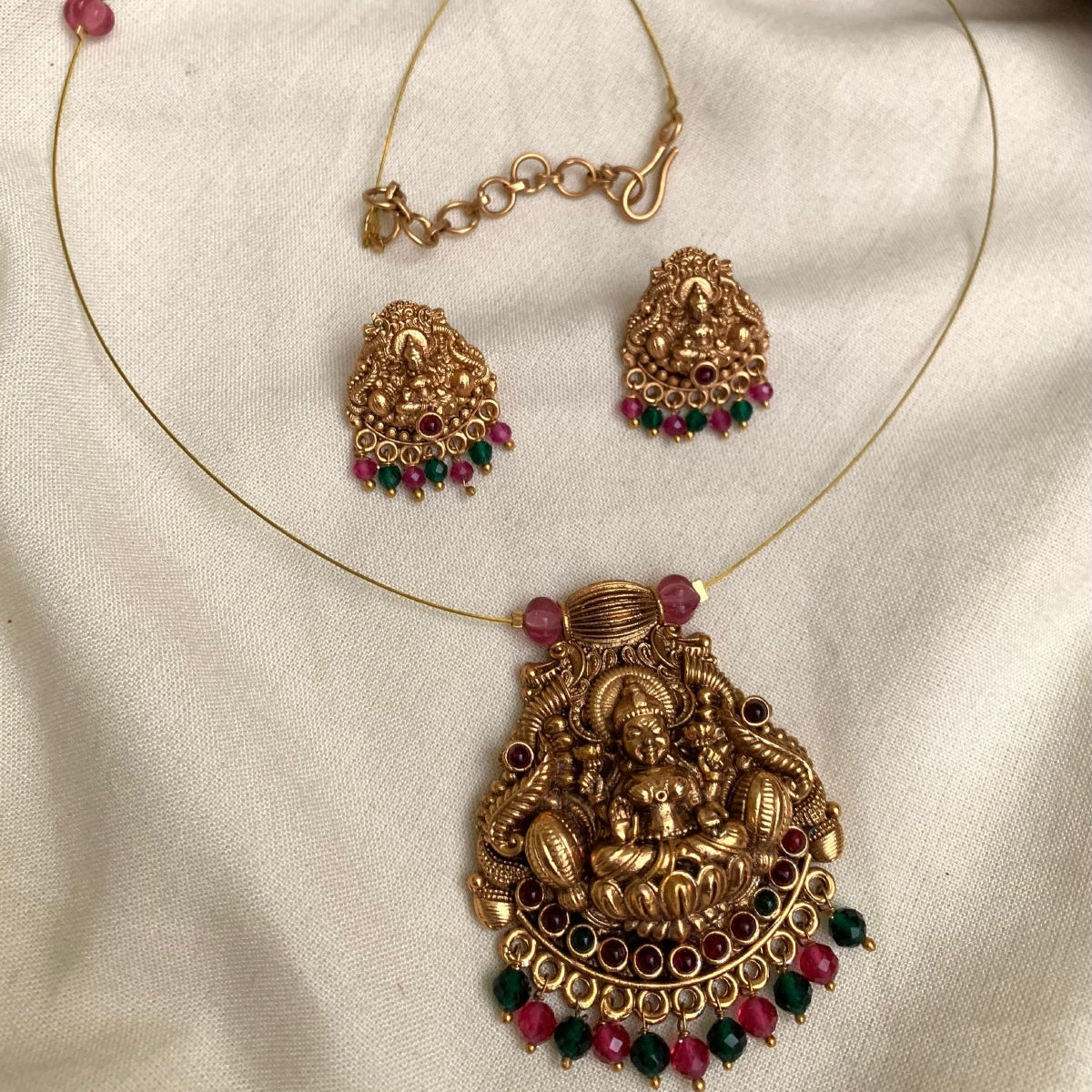Gold necklace with pendant and matching earrings on a white fabric background