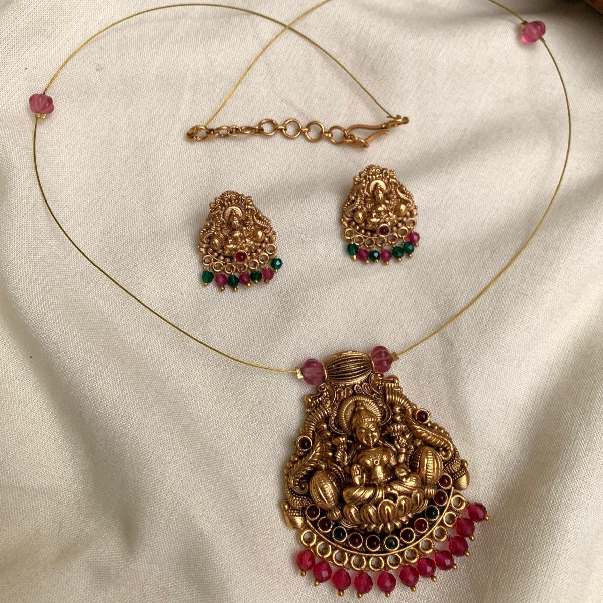Gold necklace with pendant and earrings on a beige fabric background