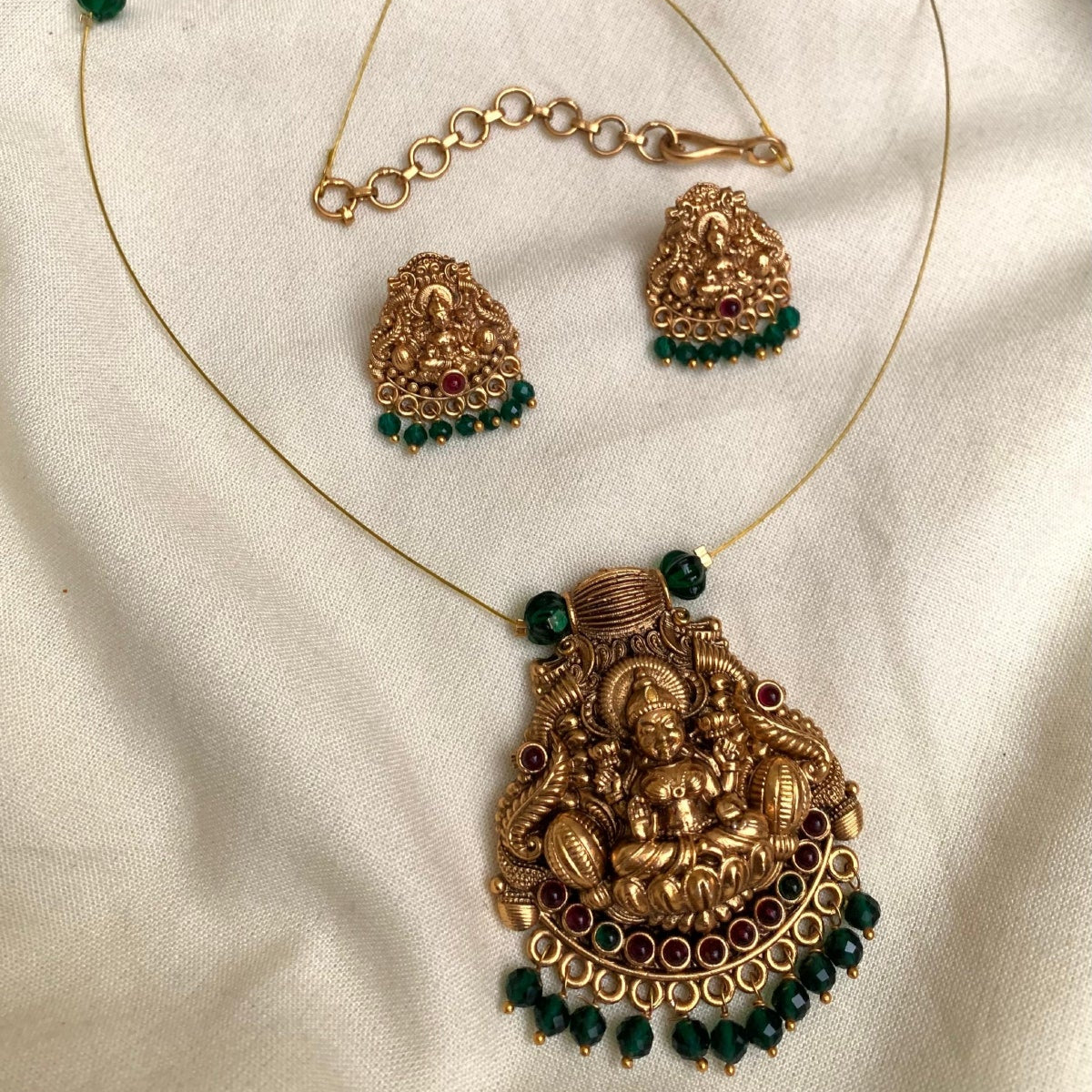 Gold necklace with pendant and matching earrings on a white fabric background