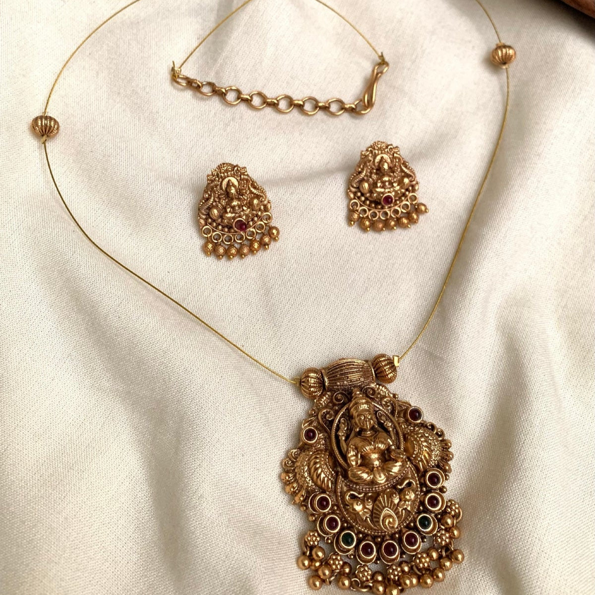 Ornate gold necklace with pendant and matching earrings on a beige fabric background