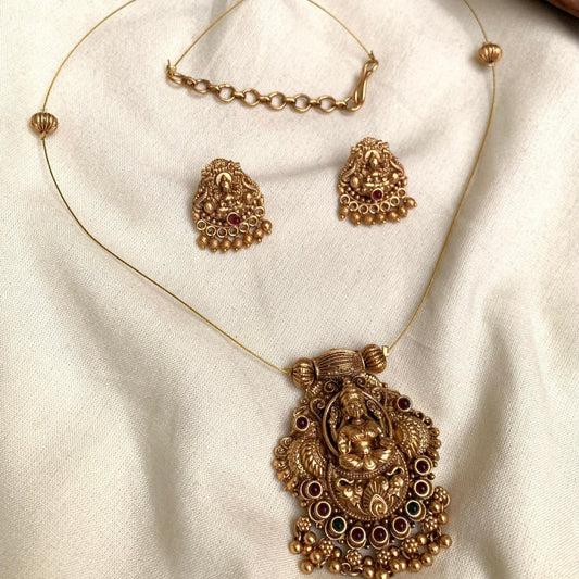 Ornate gold necklace with pendant and matching earrings on a beige fabric background