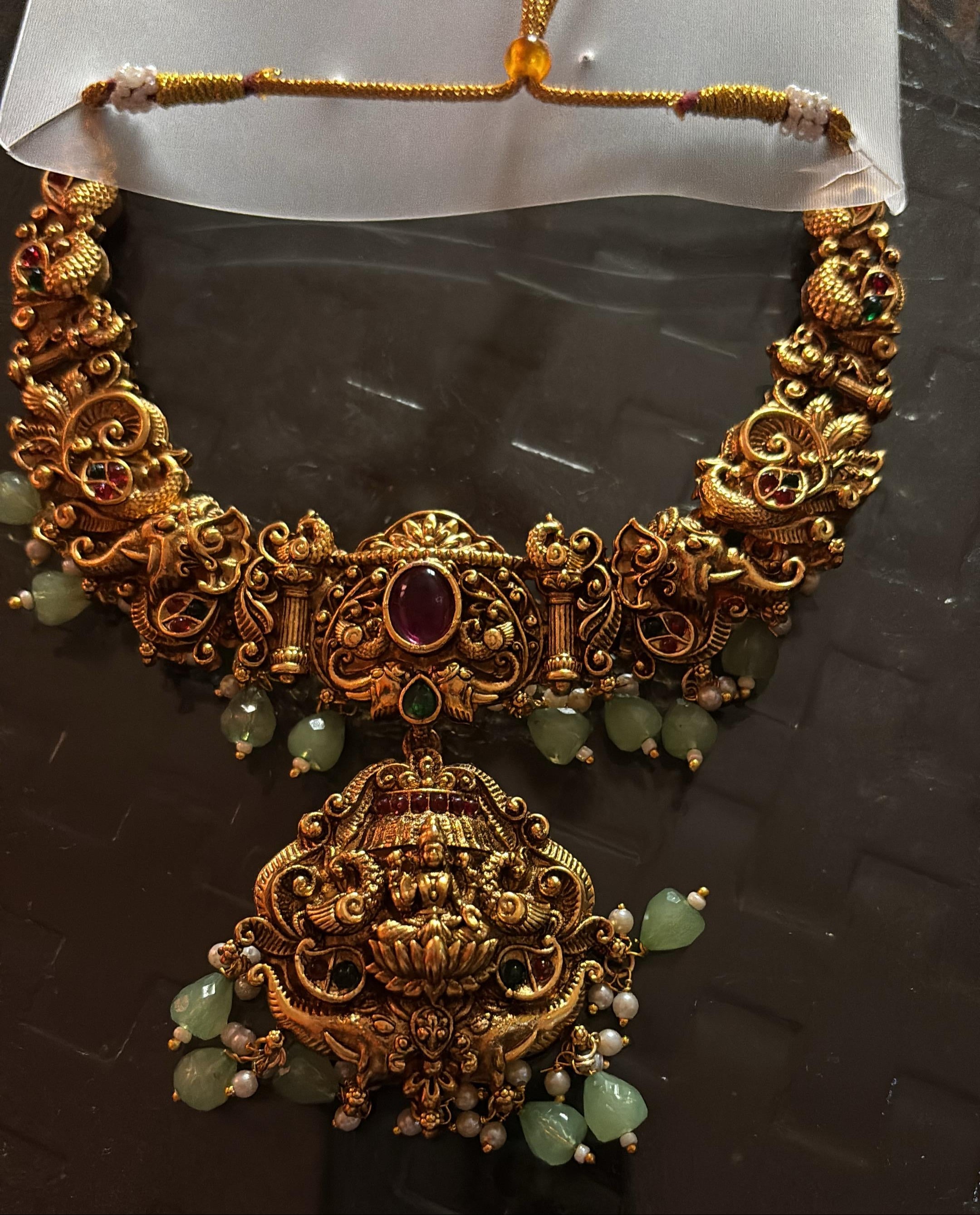 Ornate gold necklace with green beads on a dark surface