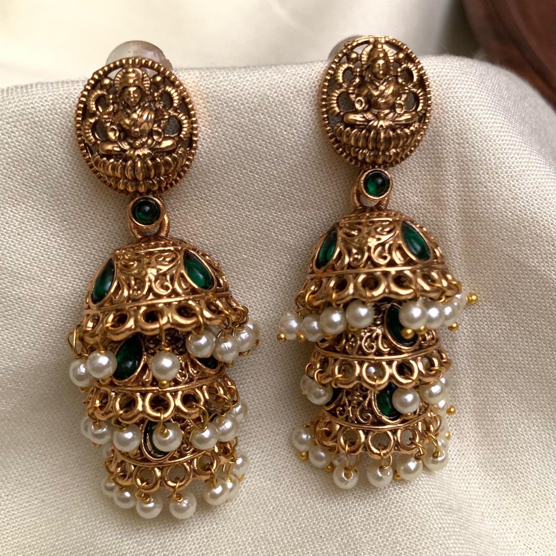 Gold earrings with pearls and green stones on a white fabric background
